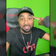 Detrick Houchens smiles while he sits in his Respawn gaming chair in front of his green screen.